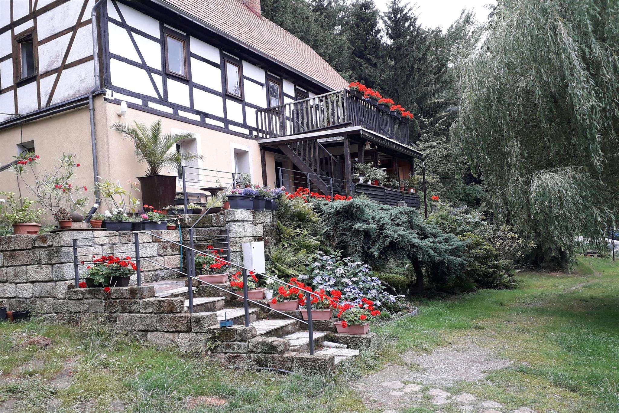 Der Ferienhof Wendt in voller Blüte – Fachwerkhaus mit blühenden Geranien, Steintreppe und Garten